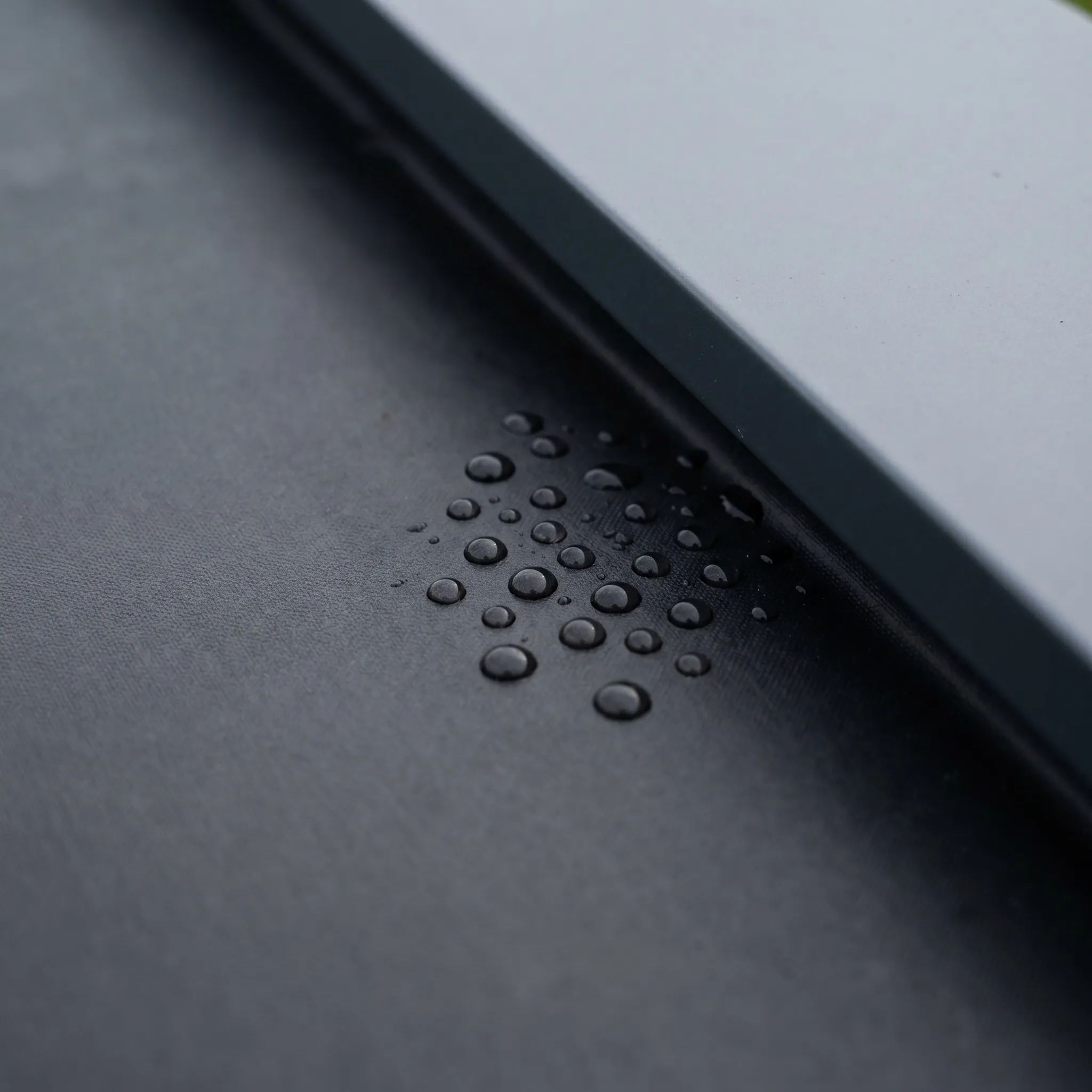 Macro of the black EPDM roof membrane meeting the drip edge, rain beading on the surface