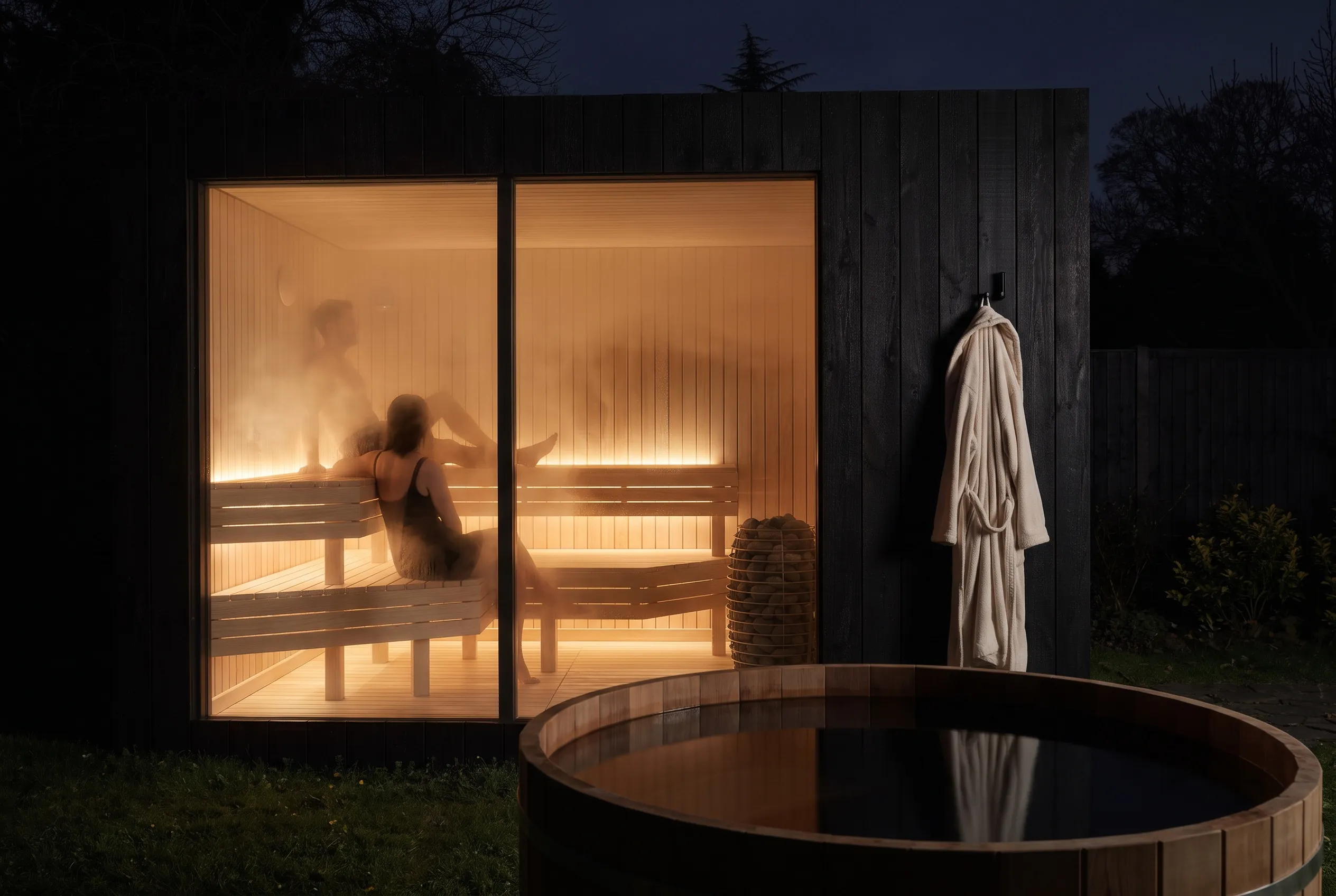 Two guests mid-session inside the lit NOOK Sauna at night, steam on the glass